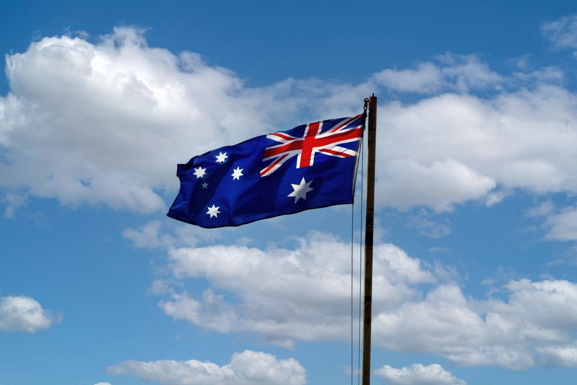 The Australian flag flying against a blue sky with clouds