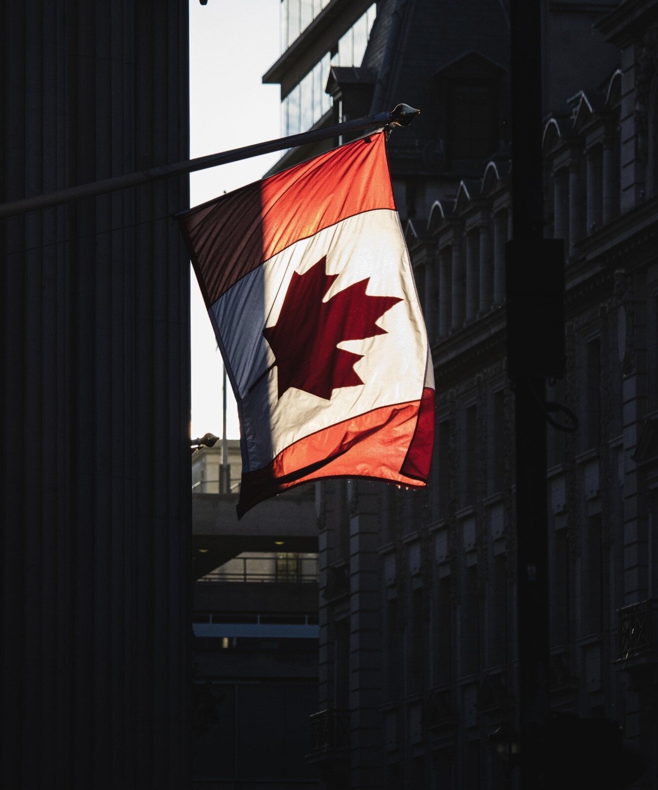 The Canadian flag lit by sunlight between city buildings
